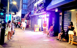 Vista nocturna de Roosevelt Avenue en Queens, reflejando la vida comunitaria y los desafíos sociales del vecindario